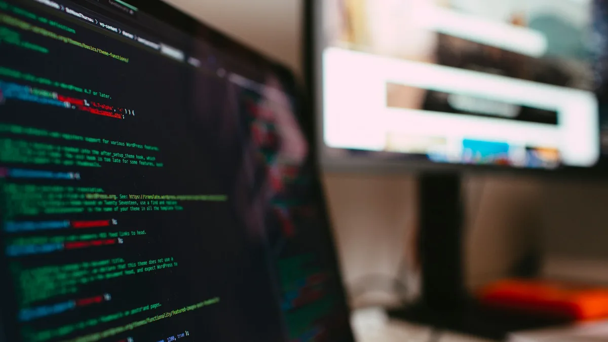Laptop und Monitor zeigen Programmcode in einer dunklen Arbeitsumgebung