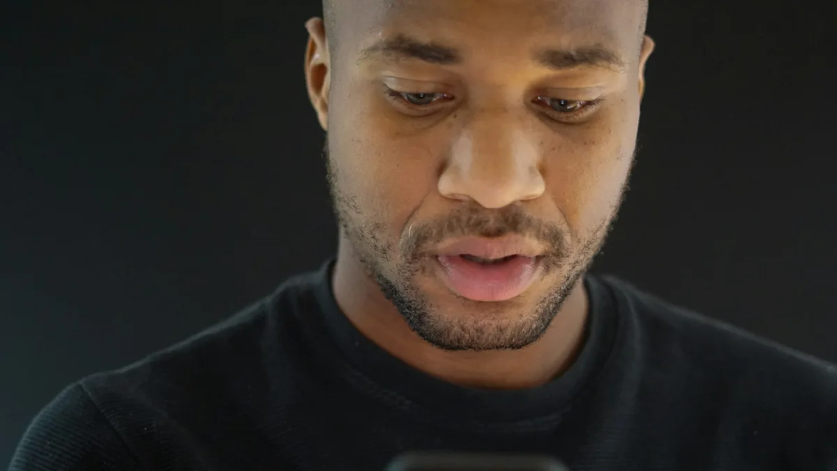 Mann blickt konzentriert auf sein Smartphone, dunkle, stimmungsvolle Beleuchtung